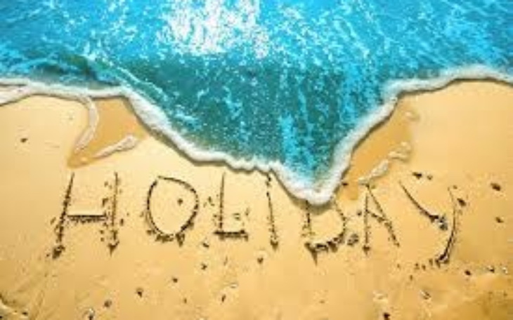 Napis 'HOLIDAY' na plaży, z falami uderzającymi w brzeg.
