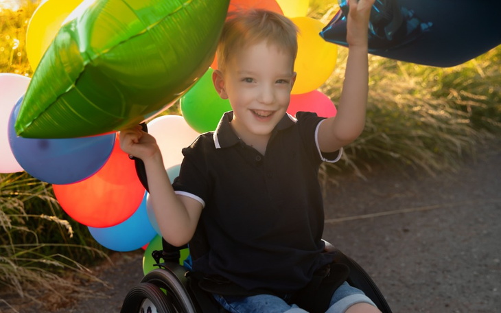Chłopiec na wózku inwalidzkim, trzymający kolorowe balony.