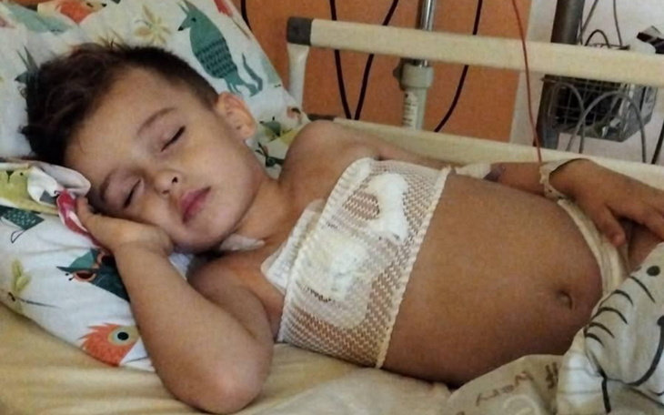 Chłopiec w szpitalu, odpoczywający po zabiegu, z opatrunkiem na brzuchu.