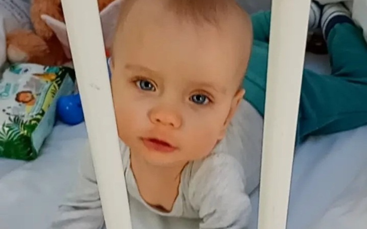 Małe dziecko patrzy przez szczebelki łóżeczka.