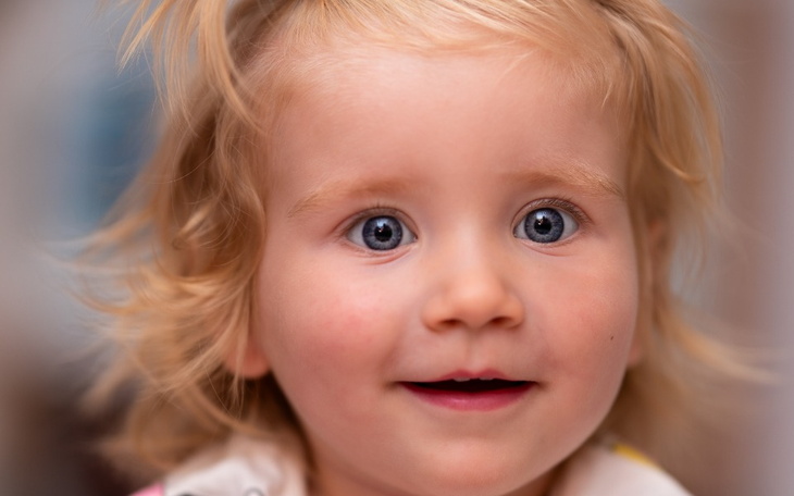 Uśmiechnięta dziewczynka z blond włosami i niebieskimi oczami.