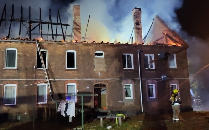 Zniszczony budynek po pożarze, z dymem w tle.