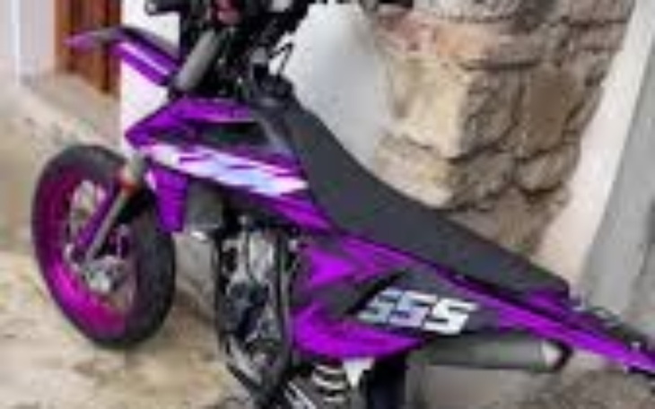 Motocykl w kolorze fioletowym zaparkowany przy ścianie.