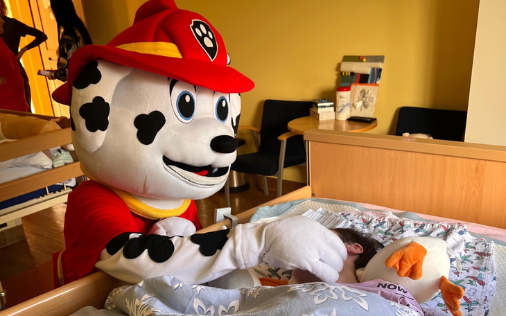 Maskotka strażaka w szpitalu, bawiąca się z dzieckiem.