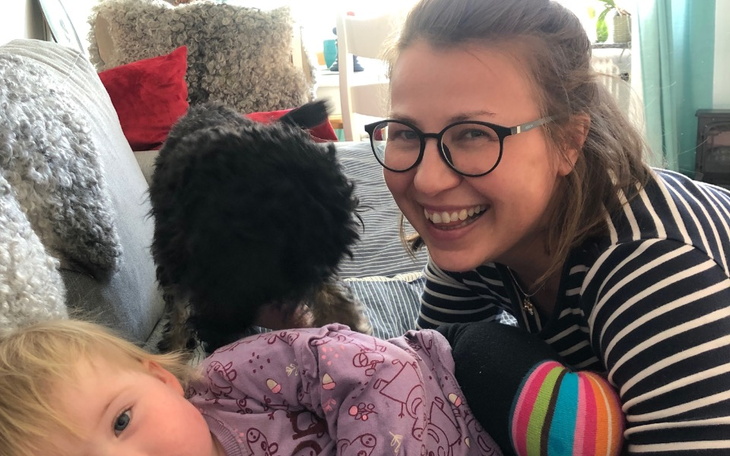 Uśmiechnięta kobieta z dzieckiem i psem na kanapie.