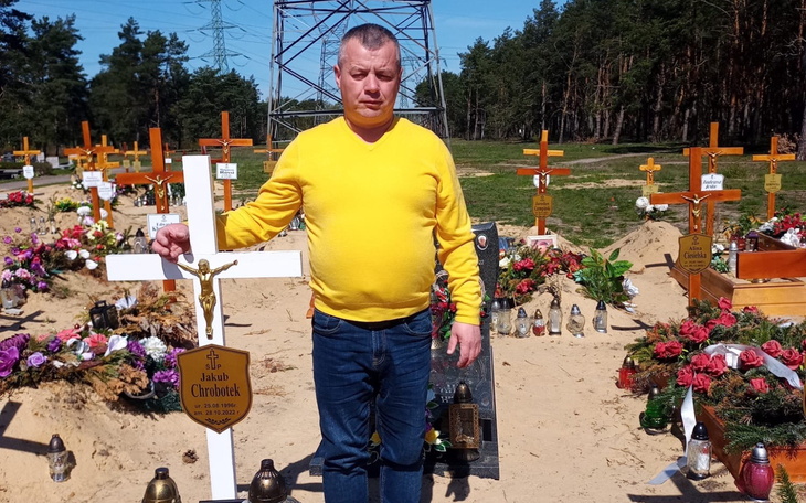 Mężczyzna przy grobie, trzymający krzyż.