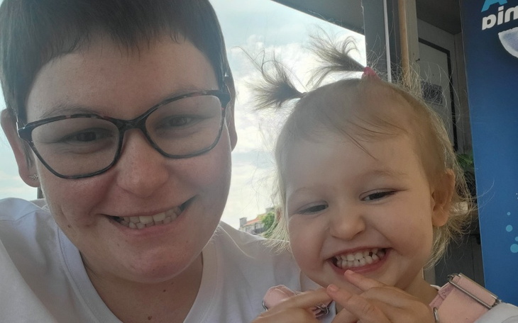 Uśmiechnięta mama z małą dziewczynką na tle nieba.