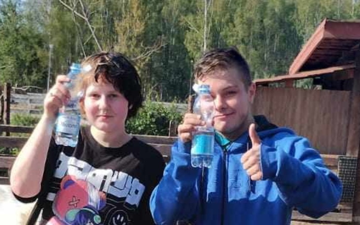 Dwoje dzieci trzyma butelki wody, uśmiechając się do kamery.