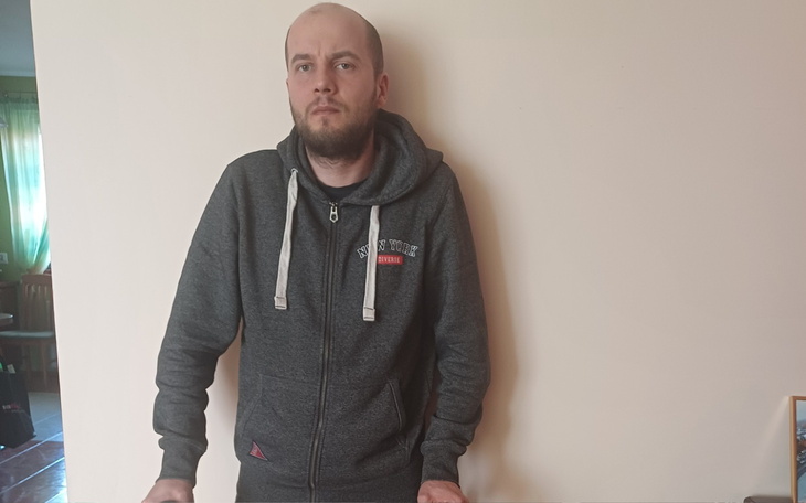 Mężczyzna w szarej bluzie, stojący przy ścianie.