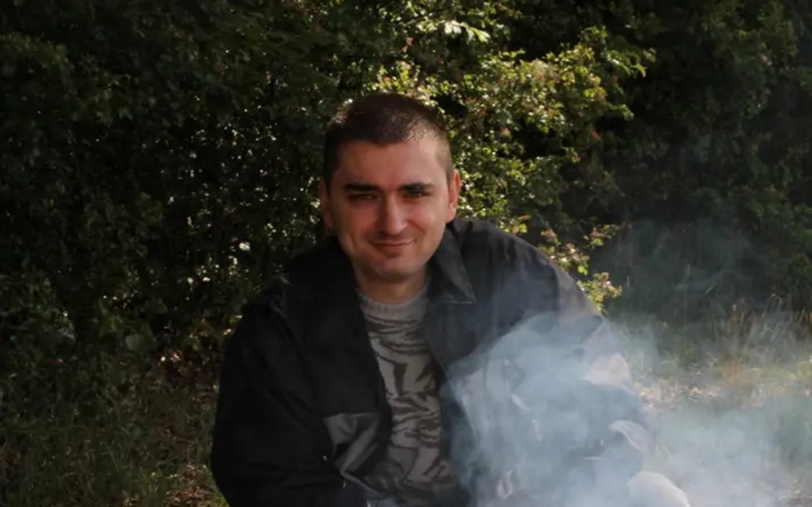 Mężczyzna siedzący przy ognisku, otoczony zielenią.