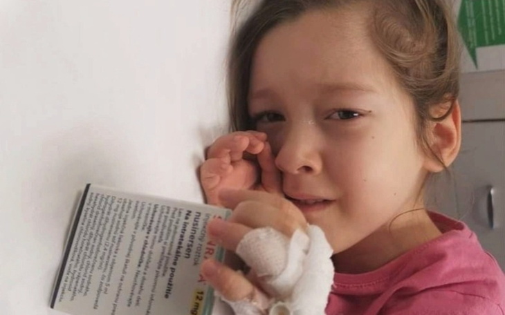 Zmartwiona dziewczynka trzymająca kartkę, z widoczną opatrunkiem ręką.