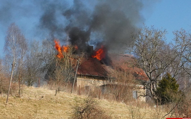 Zniszczony dom w ogniu, dym i płomienie wydobywają się z dachu.