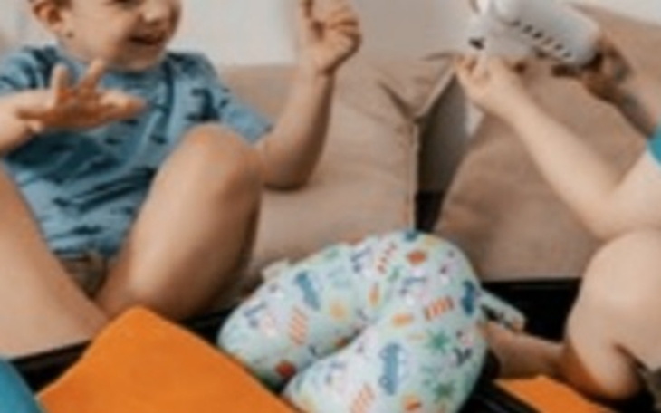 Dzieci bawią się na kanapie, obok poduszka w kształcie litery C.