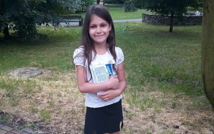 Dziewczynka w parku, trzymająca książki w ramionach.