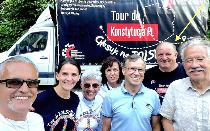 Uczestnicy wydarzenia z banerem w tle, uśmiechnięci i zadowoleni.