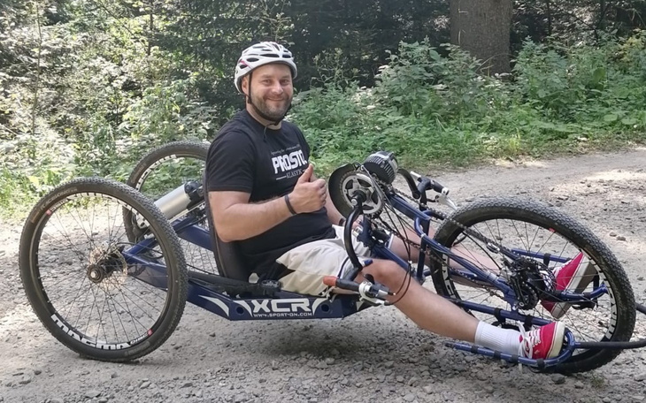 Mężczyzna na rowerze ręcznym, uśmiechający się do kamery.