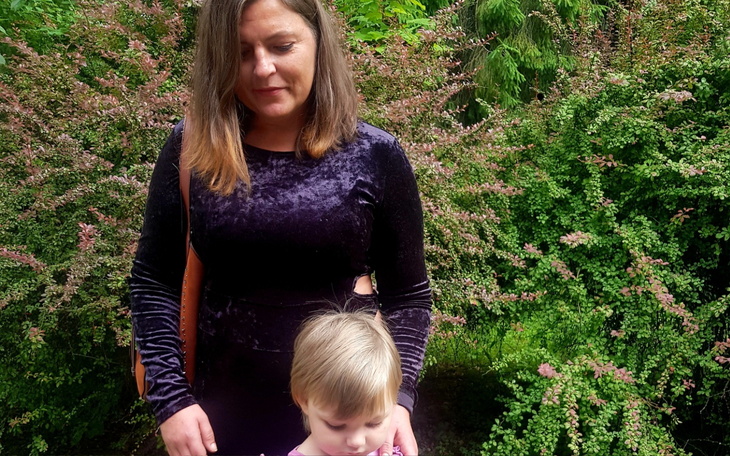 Kobieta z dzieckiem w ogrodzie, otoczona zielenią.