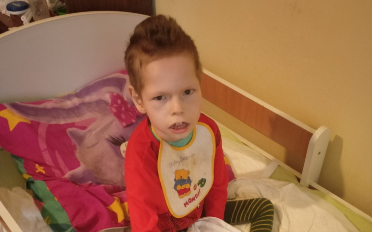 Chłopiec siedzący na łóżku, w kolorowej piżamie, z wyrazem twarzy.