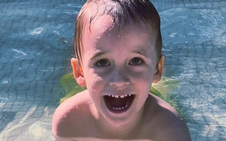 Chłopiec uśmiechający się w basenie, z wodą na twarzy.