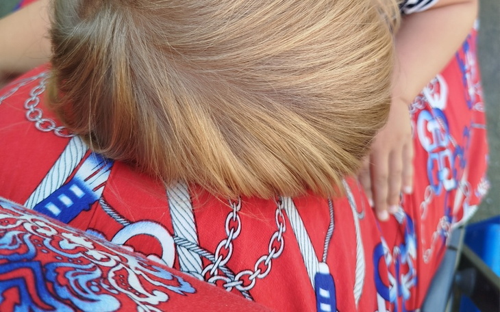 Dziecko śpi na kolanach dorosłego, w tle kolorowy materiał.