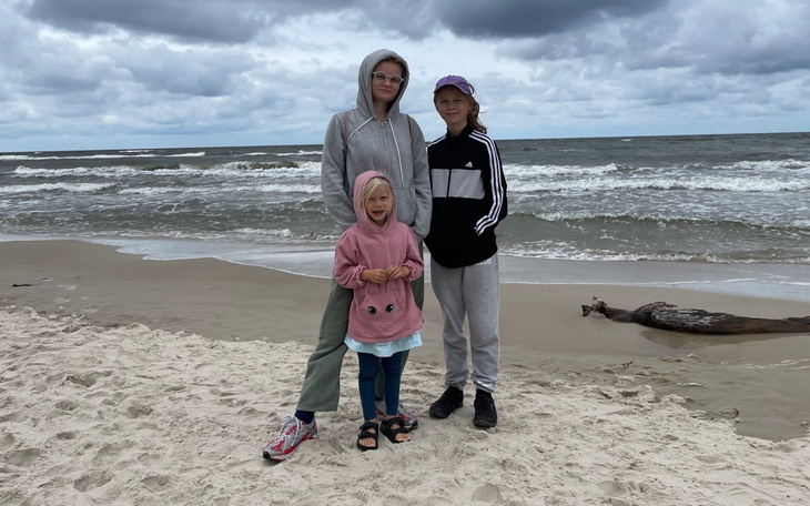 Trzy osoby na plaży, w tle fale i chmury.