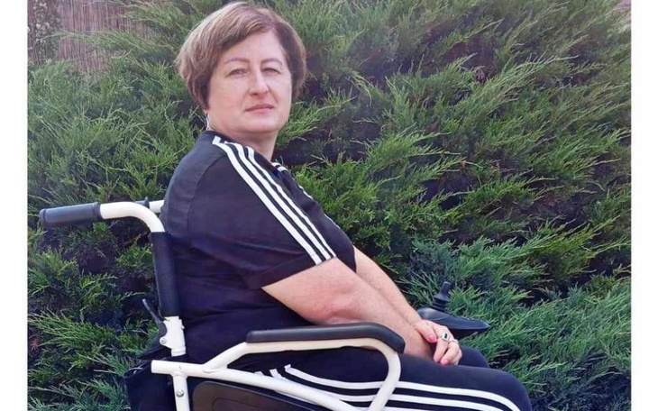 Kobieta na wózku inwalidzkim, ubrana w sportowy strój, siedzi w otoczeniu zieleni.