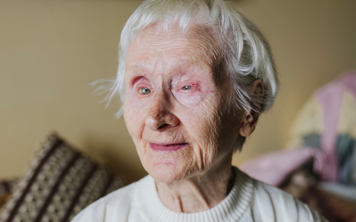 Starsza kobieta z uśmiechem, siedząca w swoim domu.