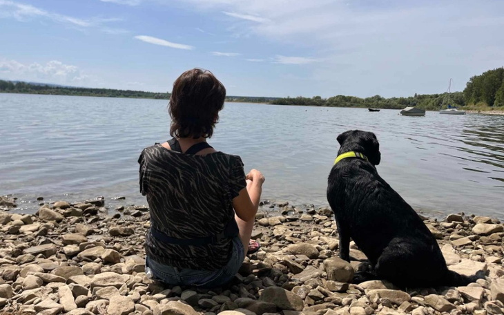 Osoba siedząca nad brzegiem wody z psem.