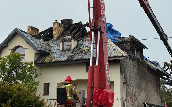 Zniszczony dach domu po pożarze, strażak na podnośniku.