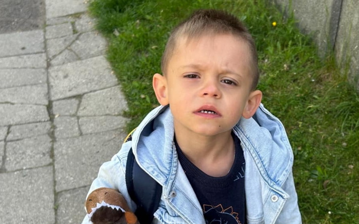 Mały chłopiec z plecakiem stoi na chodniku.