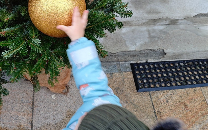 Dziecko sięga po złotą bombkę na choince.