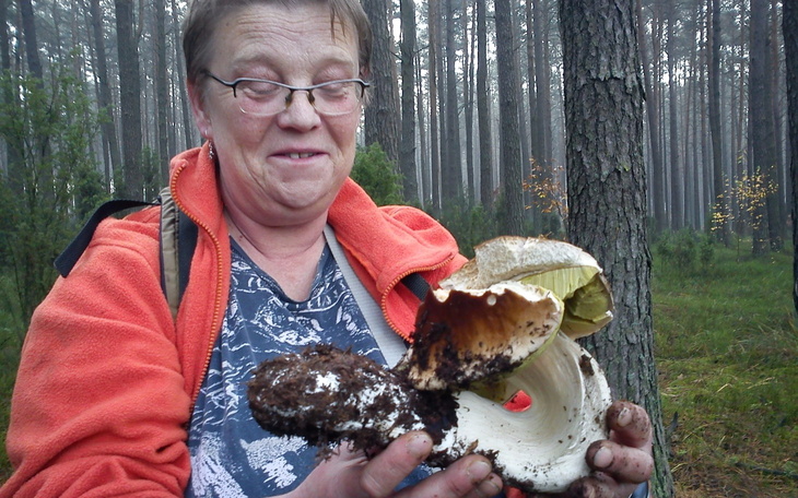 Kobieta trzymająca dużego grzyba w lesie.