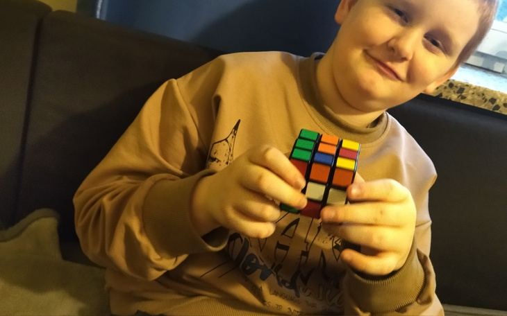 Chłopiec trzymający kostkę Rubika, uśmiechający się do kamery.