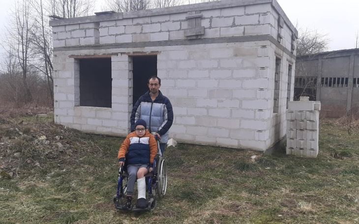 Chłopiec na wózku inwalidzkim przed budynkiem w budowie.