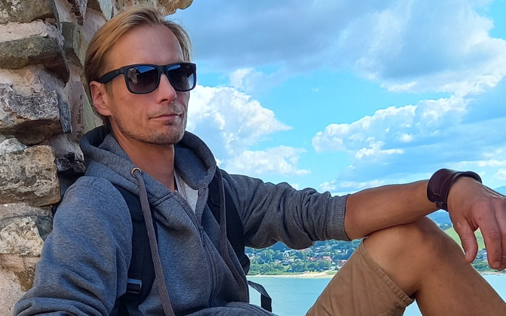 Mężczyzna w szarej bluzie siedzi na murze z widokiem na miasto.