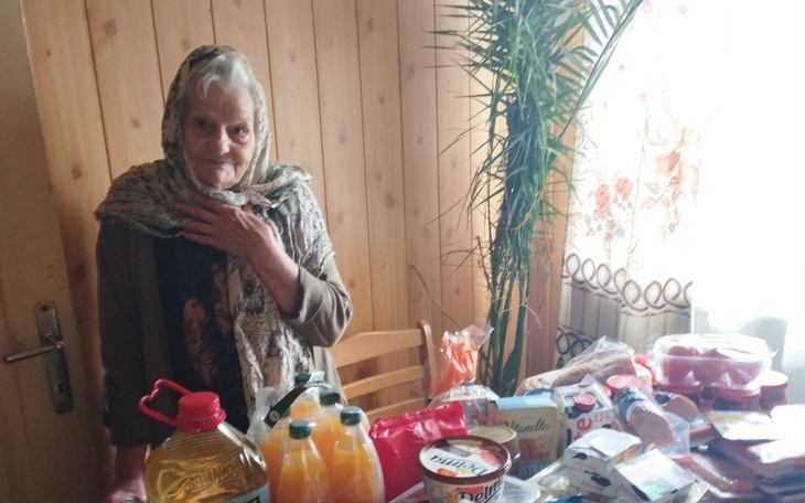 Starsza kobieta przy stole z jedzeniem i napojami.