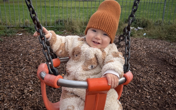 Dziecko na huśtawce, uśmiechnięte w ciepłym ubraniu.