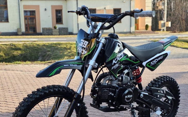 Motocykl terenowy z zielonymi akcentami, stojący na chodniku.