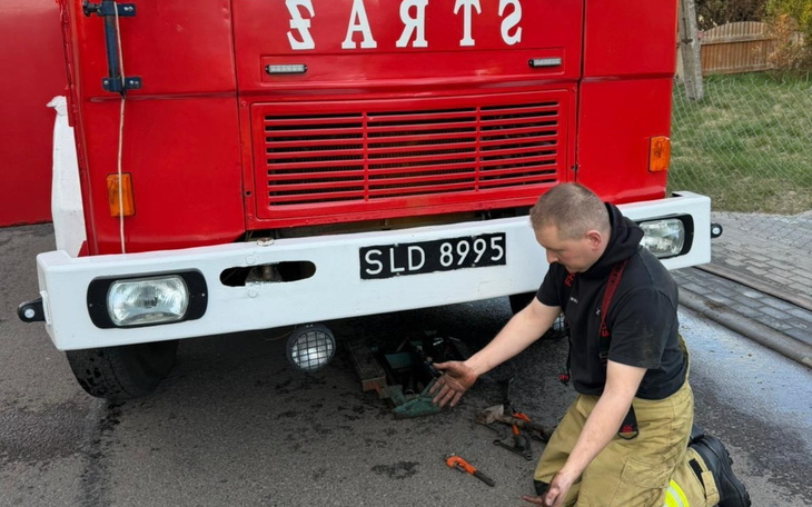 Mężczyzna naprawiający pojazd strażacki na drodze.