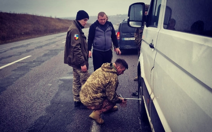 Grupa mężczyzn naprawiających oponę w samochodzie na drodze.