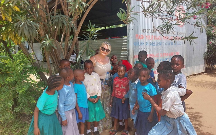 Dzieci z uśmiechami pozujące z dorosłą osobą w tle.