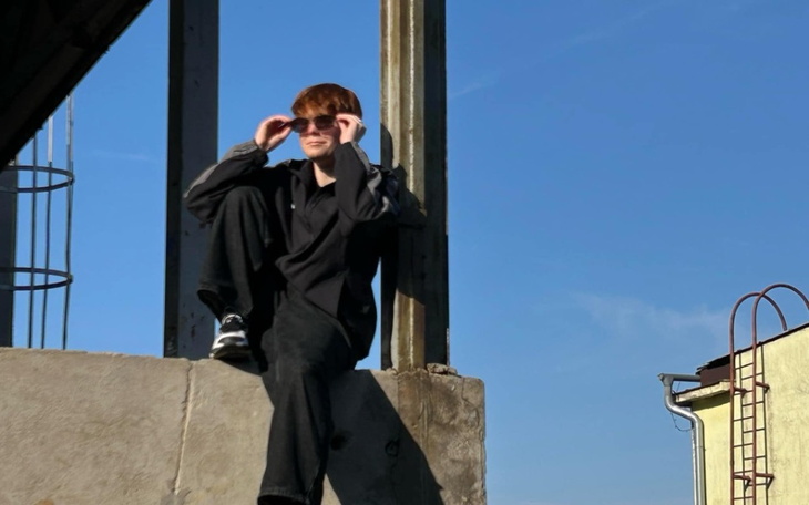 Młody mężczyzna w czarnych okularach siedzący na murze.