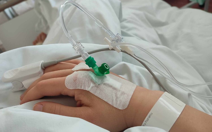 Ręka pacjenta z kroplówką w szpitalnym łóżku.