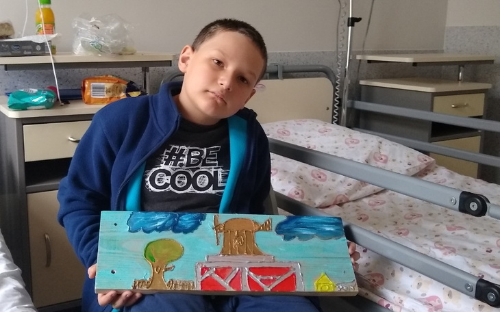 Chłopiec w szpitalu trzymający własnoręcznie wykonaną pracę.