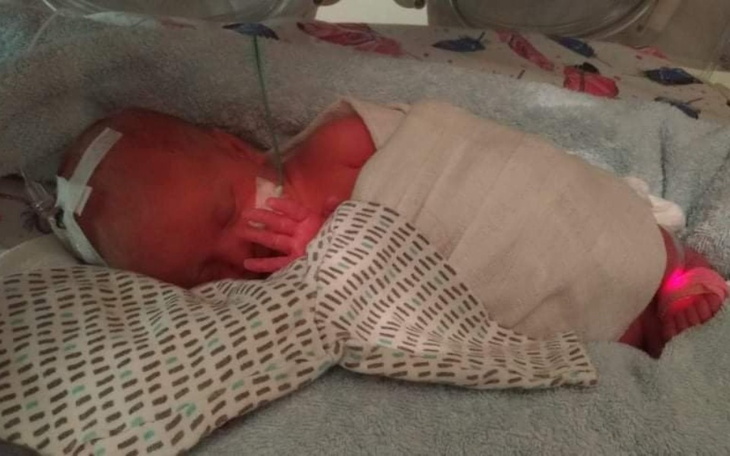 Noworodek w inkubatorze, z rurką tlenową i kocykiem.