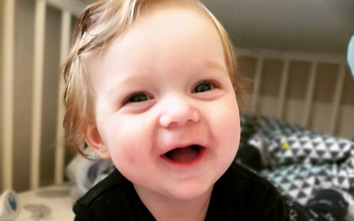 Uśmiechnięte dziecko w łóżeczku, pełne radości.