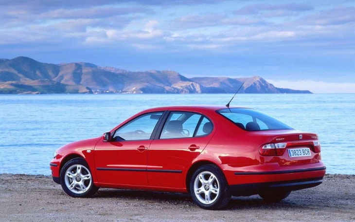 Czerwony samochód zaparkowany nad brzegiem morza, w tle góry.