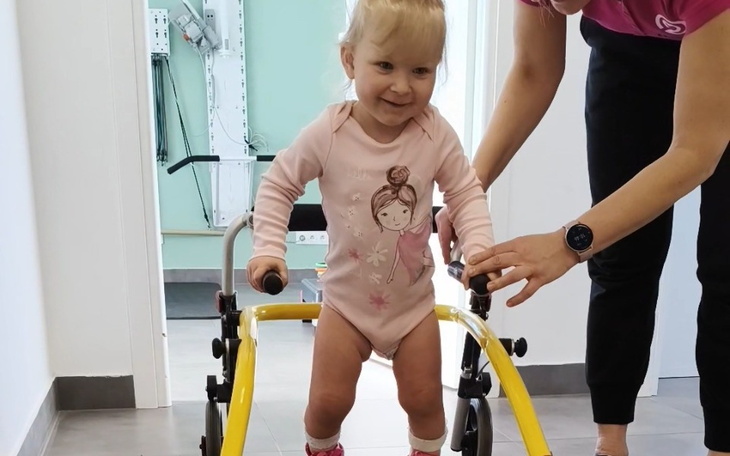 Mała dziewczynka uczy się chodzić z pomocą wózka.