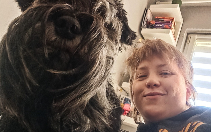 Osoba z psem, uśmiechnięta w domowym otoczeniu.