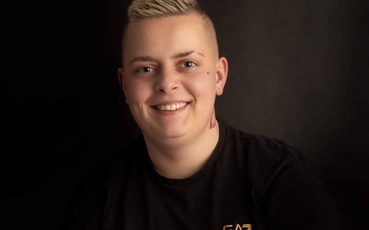 Uśmiechnięta osoba z krótkimi włosami na ciemnym tle.